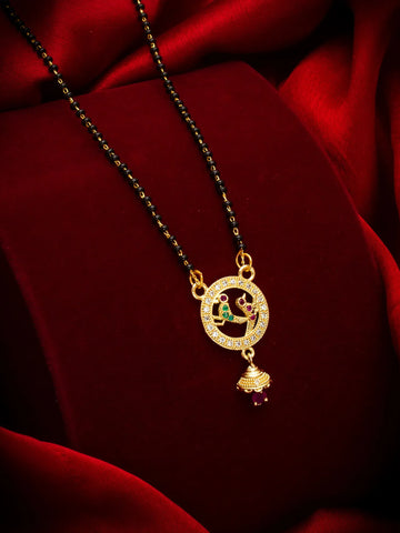 Gold-plated necklace with a circular pendant featuring a peacock and a dangling bell charm, displayed on a deep red velvet background.