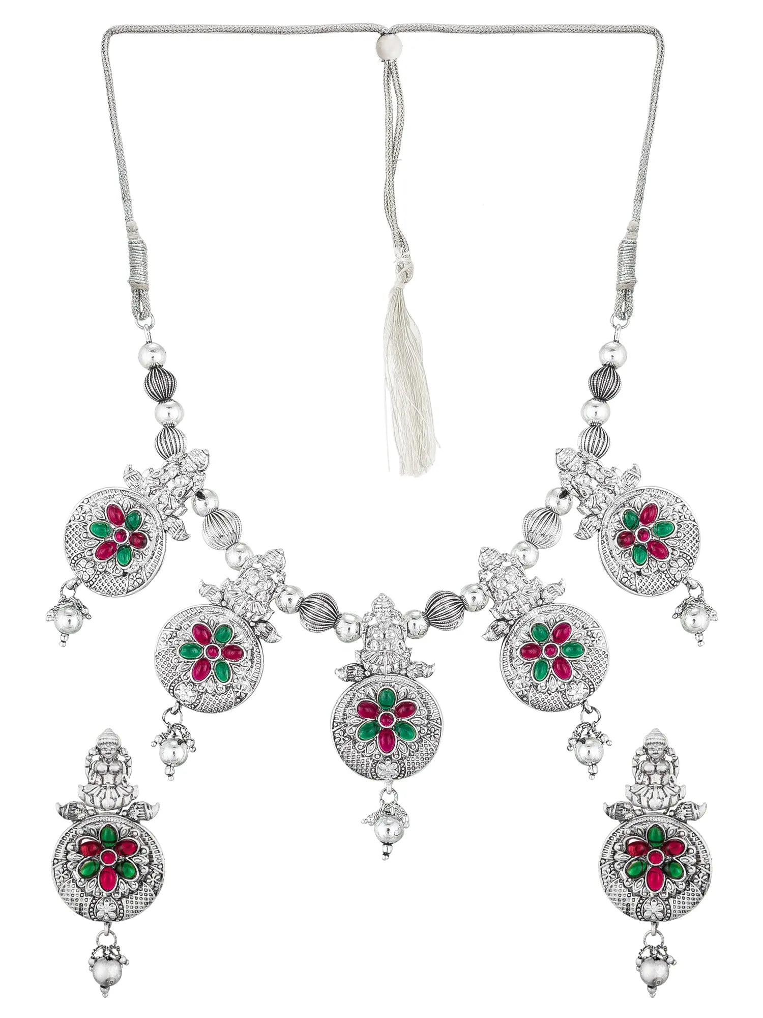 Silver-toned traditional Indian jewelry set featuring a necklace and matching earrings with ornate filigree work and floral motifs in red and green stones.