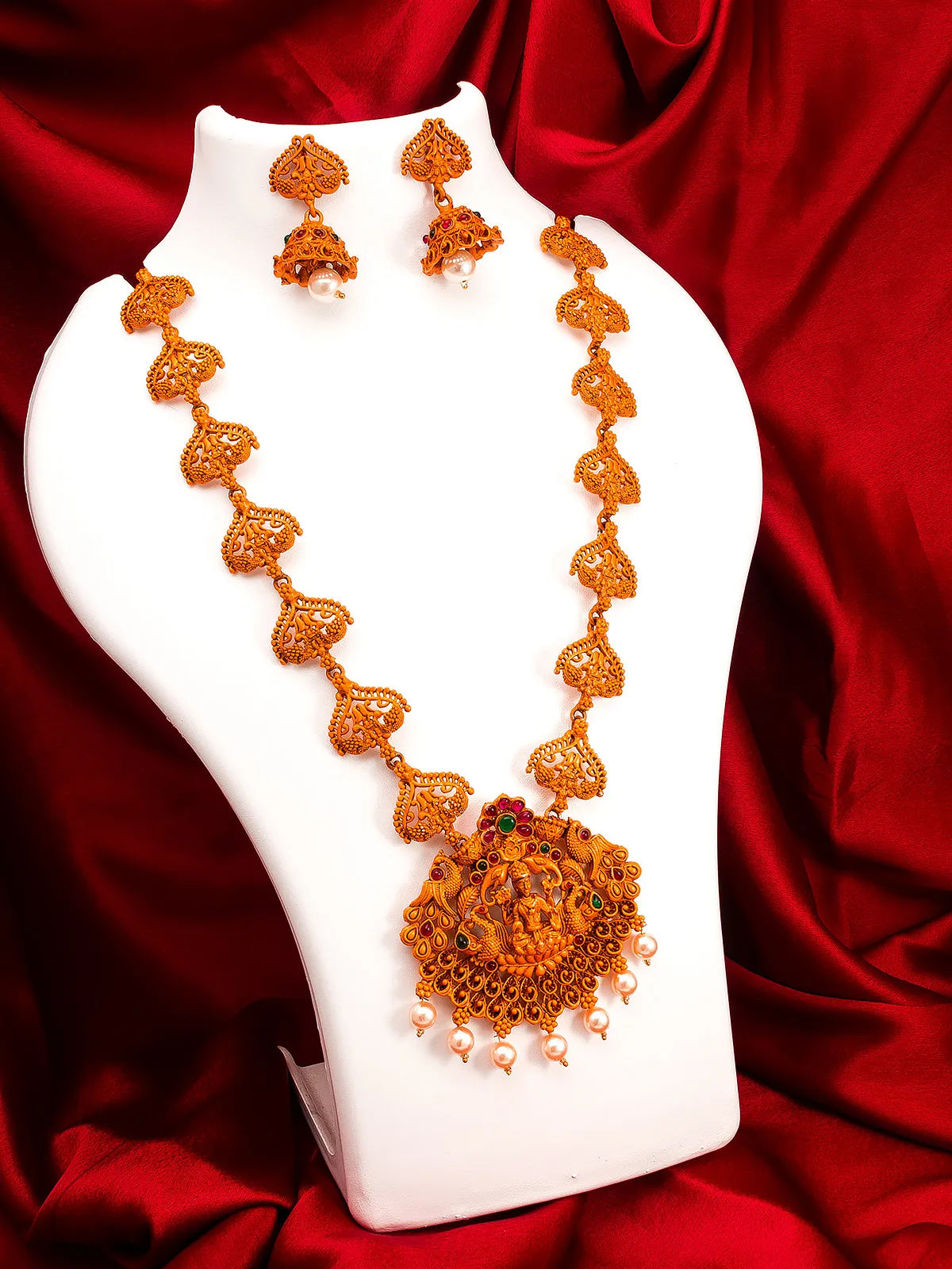 Ornate necklace and earrings on a white stand with a red fabric background