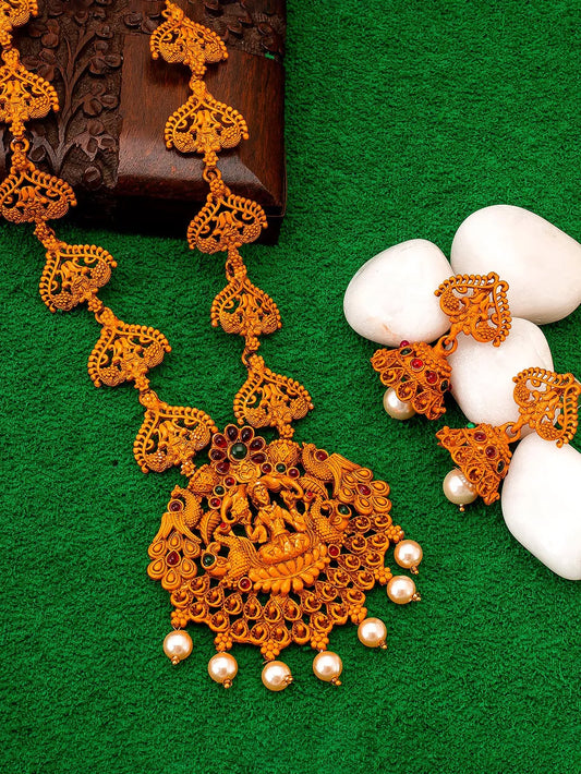 Ornate gold necklace with pearl beads and matching earrings on a green surface.