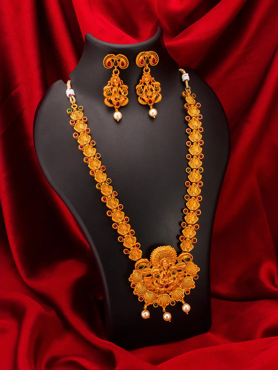 Gold-toned traditional jewelry set including a necklace, matching earrings, and a black display bust against a draped red fabric background.