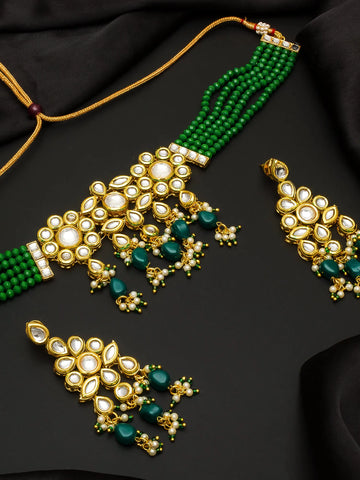 Gold and green traditional Indian jewelry set featuring a necklace, earrings, and a choker with white stones and green beads, arranged on a black fabric background.