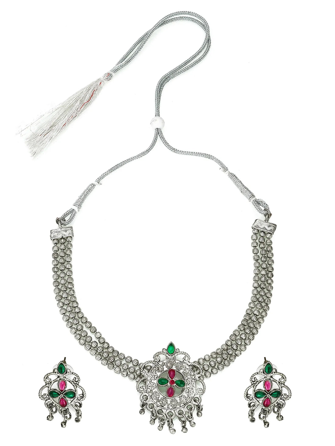 Silver jewelry set with red and green stones on a red fabric background