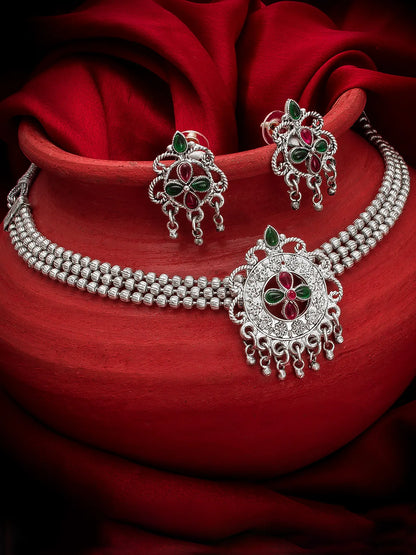 Silver jewelry set with red and green stones on a red fabric background