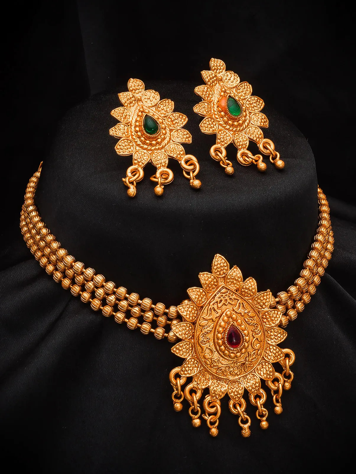 Gold-toned traditional jewelry set featuring a multi-strand necklace with an ornate pendant, matching earrings, and a black display bust.