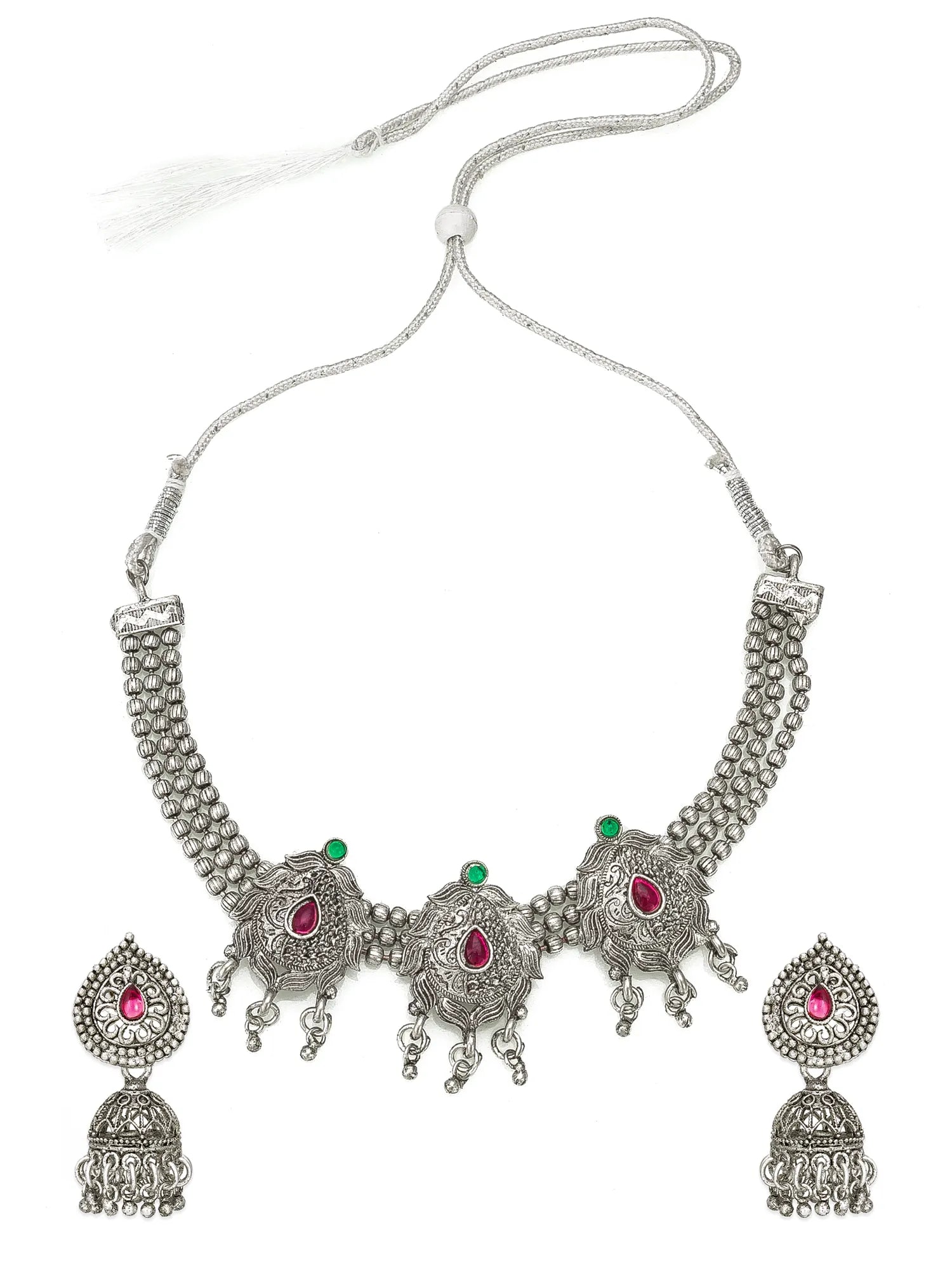 A traditional Indian silver-toned jewelry set featuring a necklace and matching earrings. The necklace has a textured silver chain with a central ornate silver pendant decorated with three red teardrop gemstones and small green stone accents.