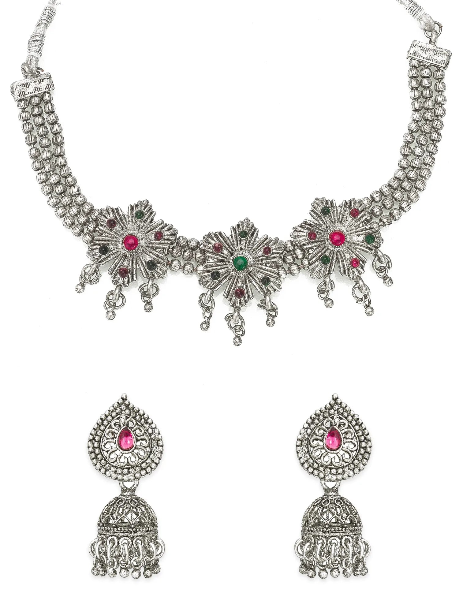 An ornate silver-toned traditional necklace with matching jhumka earrings, featuring silver floral motifs set with pink and green stones, suspended from a silver cord with a tassel, on a plain white background.