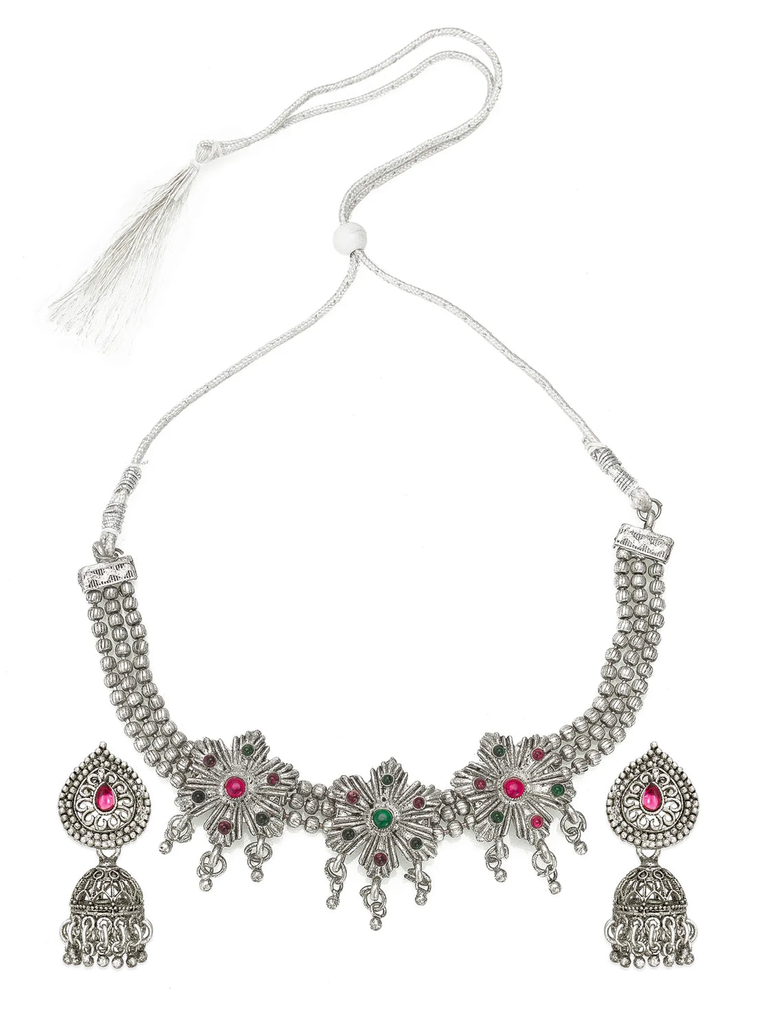 An ornate silver-toned jewelry set displayed on a black fabric background, including a choker necklace and matching earrings. The pieces feature intricate filigree detailing, beaded borders, and red and green stone accents.