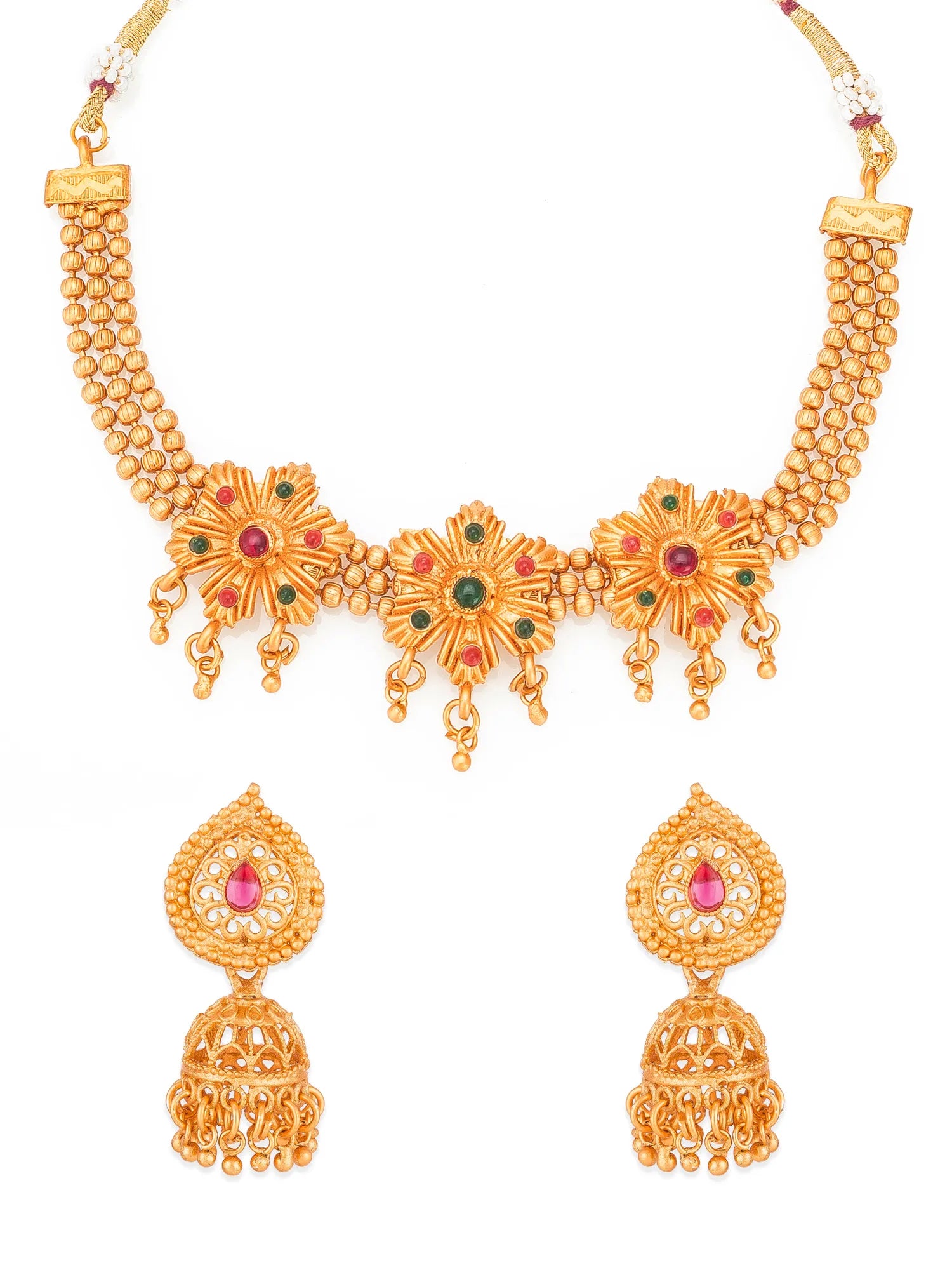 Gold-plated traditional Indian jewelry set featuring a necklace and matching earrings with floral motifs, red and green stone accents, and dangling jhumka bells, shown on a plain white background.