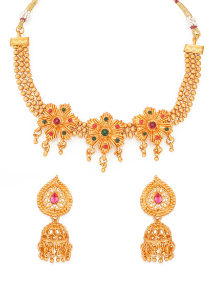 Gold-plated traditional Indian jewelry set featuring a necklace and matching earrings with floral motifs, red and green stone accents, and dangling jhumka bells, shown on a plain white background.