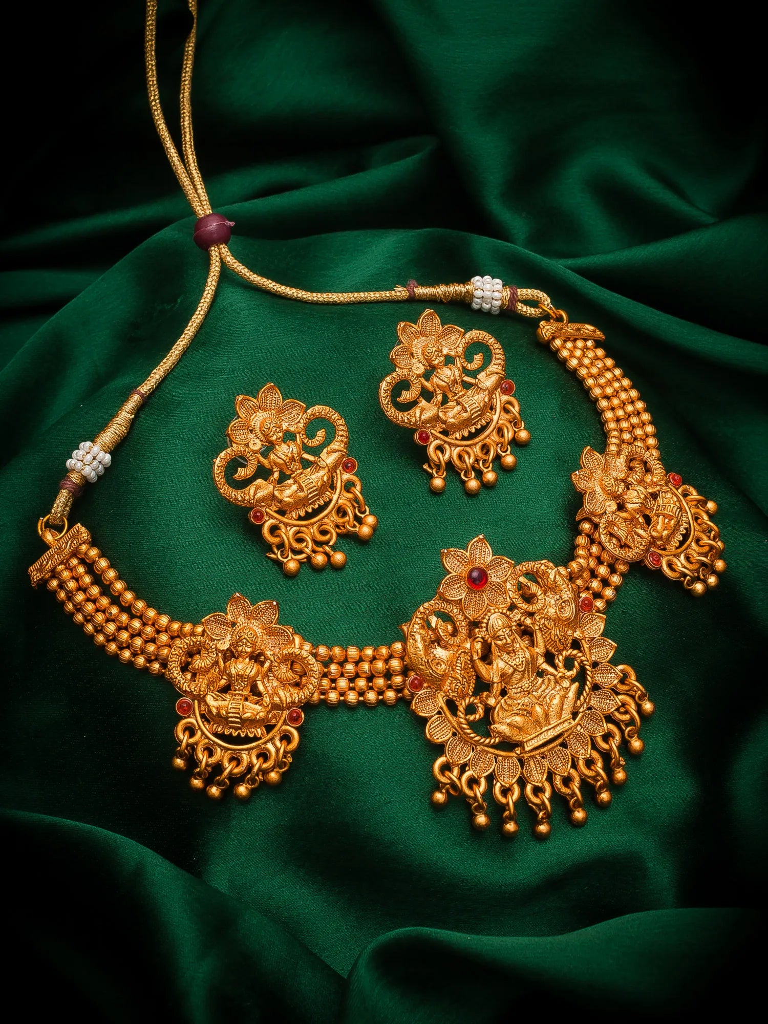 An ornate gold-toned traditional jewelry set displayed on draped dark green satin fabric, including a necklace, earrings, and matching pendant pieces with floral and filigree details.