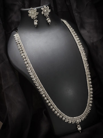 A silver-toned traditional Indian jewelry set featuring a necklace, matching earrings, and a bracelet displayed on a black mannequin bust against a black fabric backdrop.