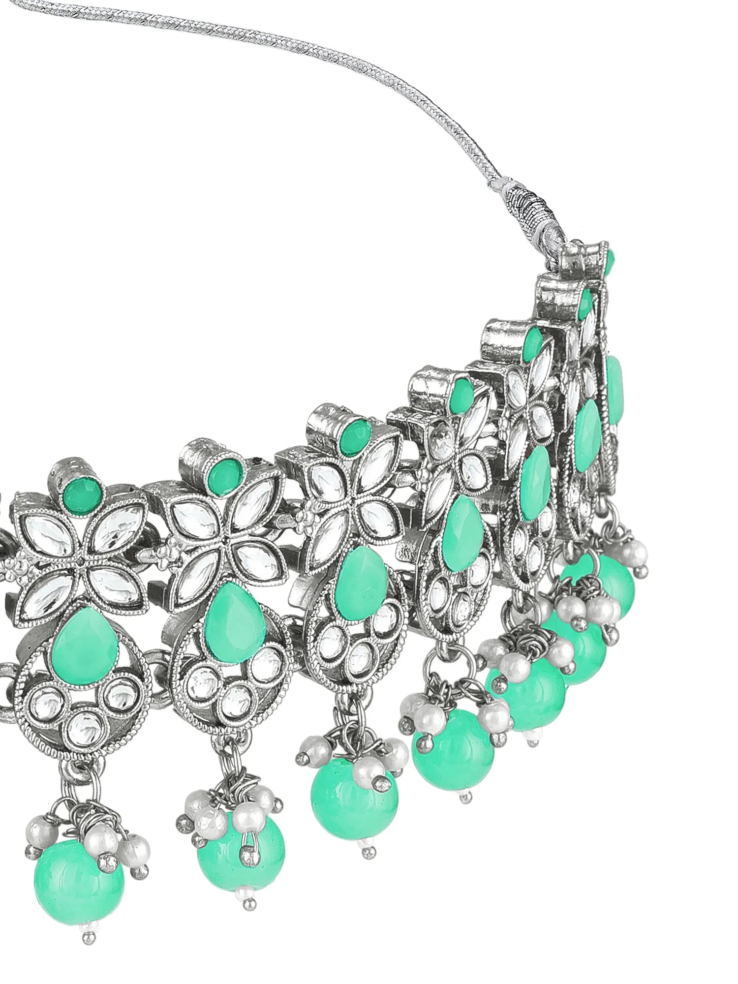 An ornate silver-toned statement necklace featuring intricate floral filigree, small clear stones, and dangling green teardrop and round beads on a white background.