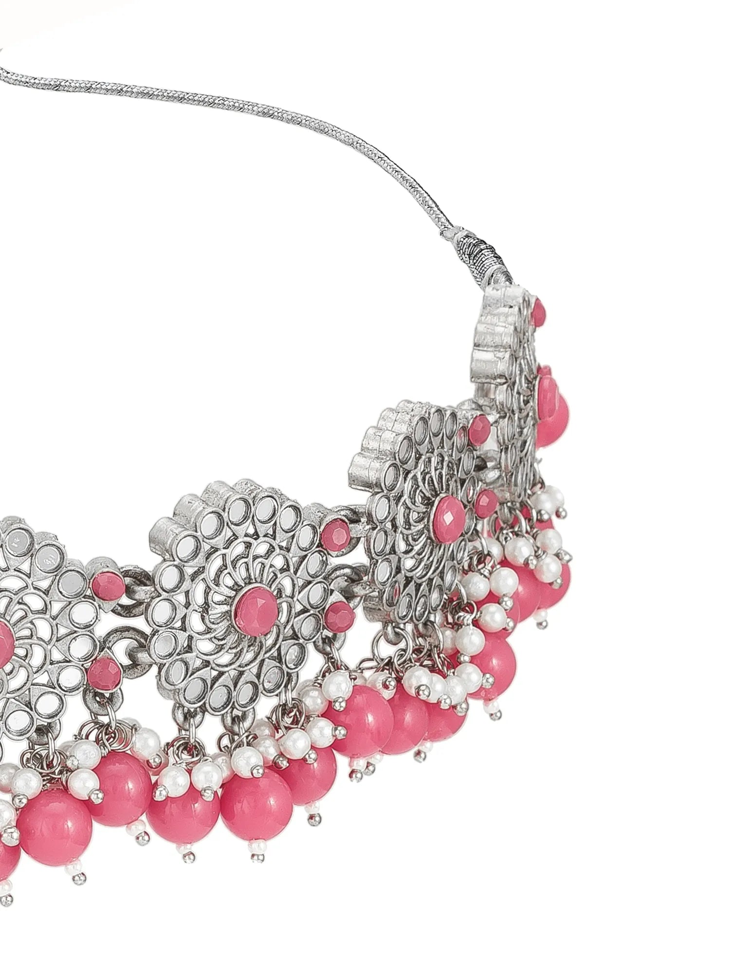 A close-up of a silver-toned statement necklace featuring intricate filigree patterns, pink beads, and dangling pink and white pearl-like accents on a white background.
