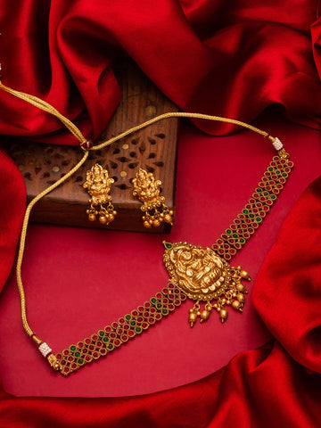 Gold-toned traditional jewelry set featuring a necklace with a detailed central pendant and matching earrings, styled on a red satin fabric background with a carved wooden block.