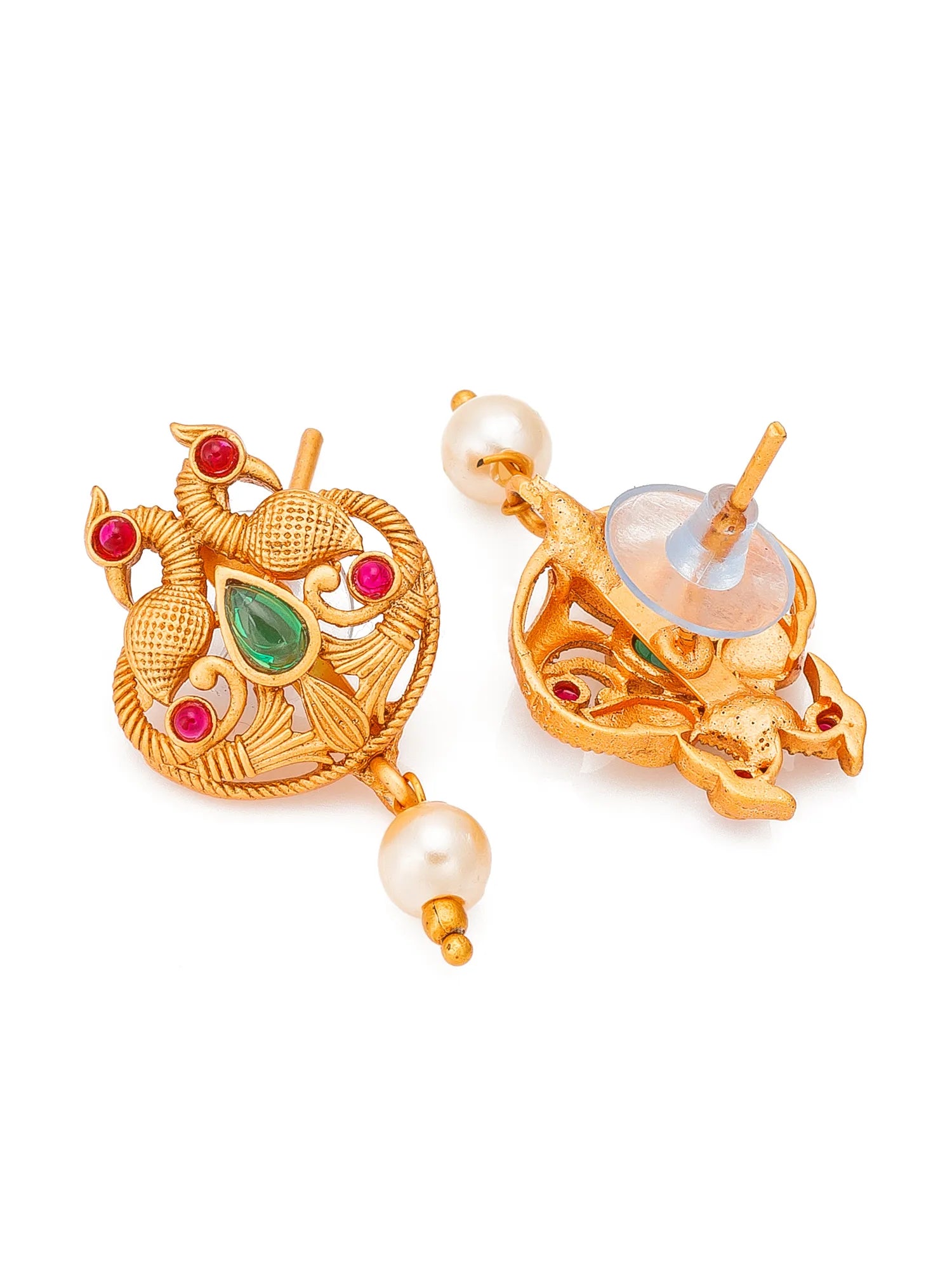 A pair of gold-toned traditional Indian earrings featuring a peacock motif with a green teardrop stone, red round stones, and a dangling white pearl, shown on a plain white background.
