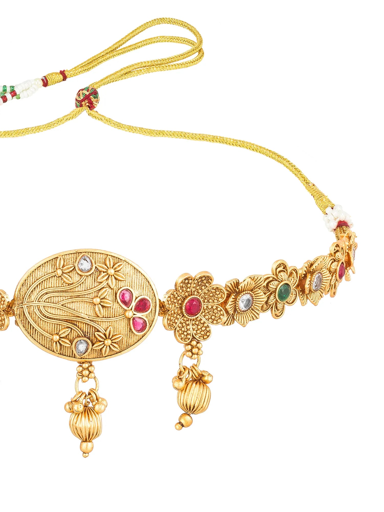 Gold-toned traditional necklace with an oval engraved centerpiece, floral motifs, dangling bell charms, and small red and green stone accents on a white background.
