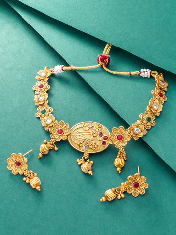 Gold-toned traditional Indian jewelry set featuring a necklace and matching earrings, embellished with red, green, and white stones on a teal background.