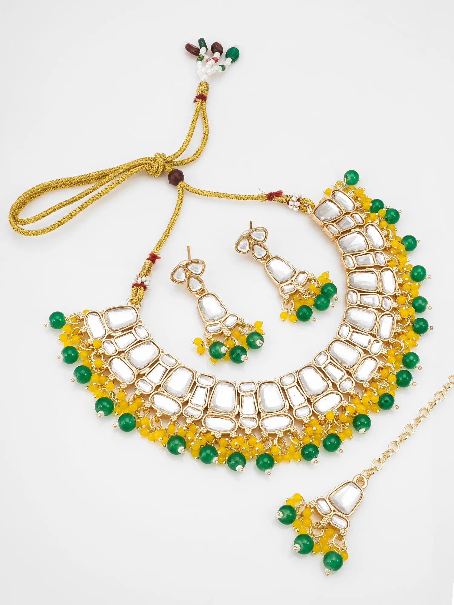 Gold-toned traditional necklace and matching earrings set with white stones, yellow floral bead accents, and green round beads on a plain light background.
