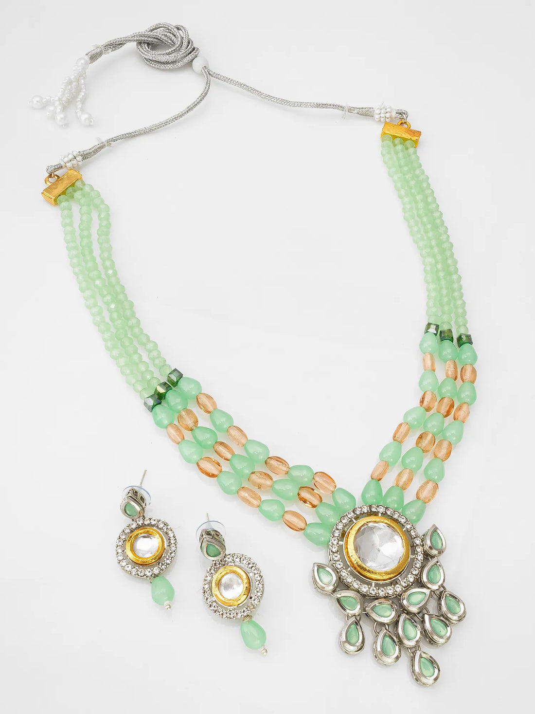 Green beaded necklace with gold accents and matching earrings on a green surface.