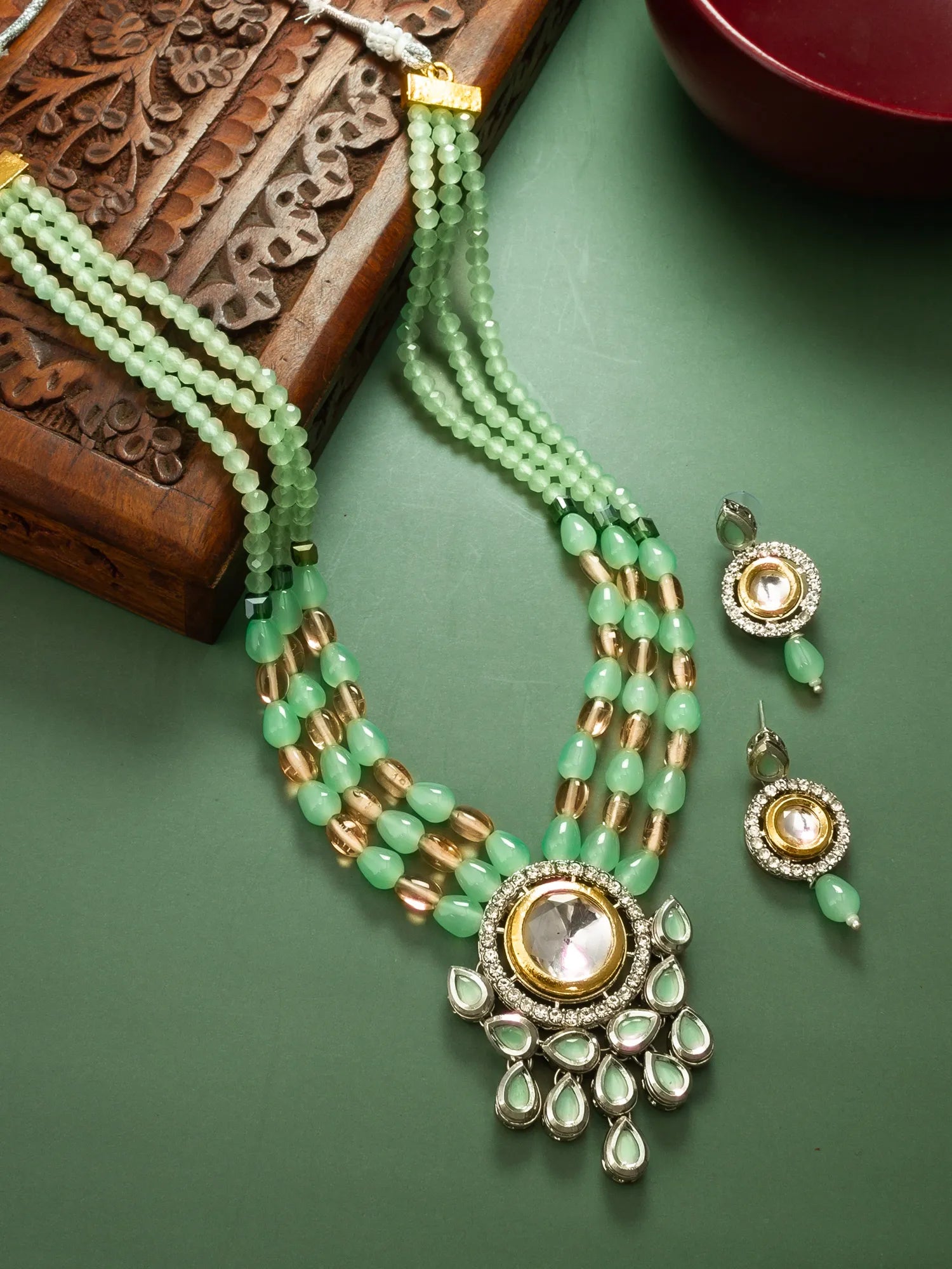Green beaded necklace with gold accents and matching earrings on a green surface.
