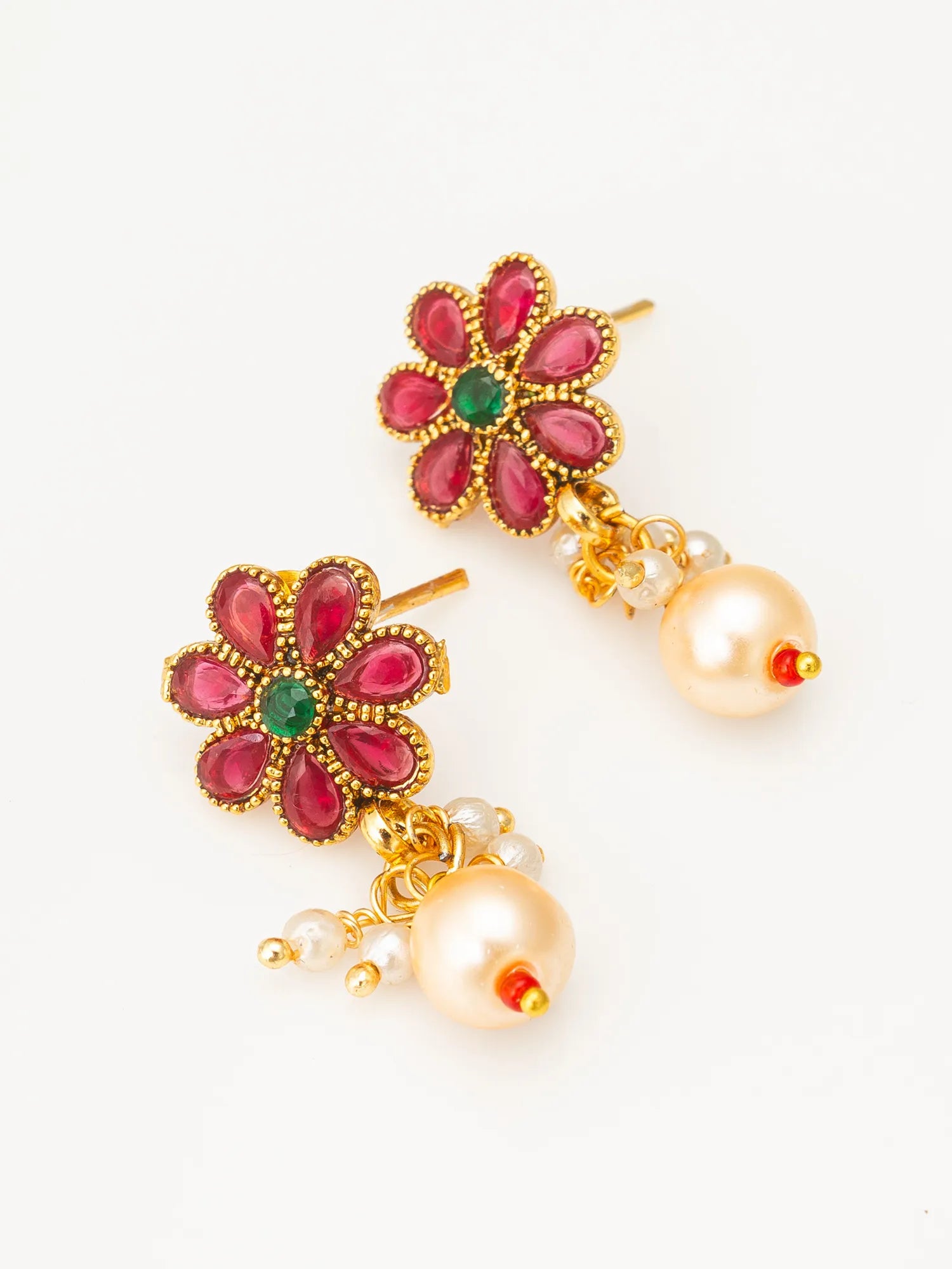 A pair of gold-plated floral dangle earrings featuring pink teardrop-shaped stones, a small green center stone, and dangling cream-colored pearls with tiny red accent beads, set against a plain white background.