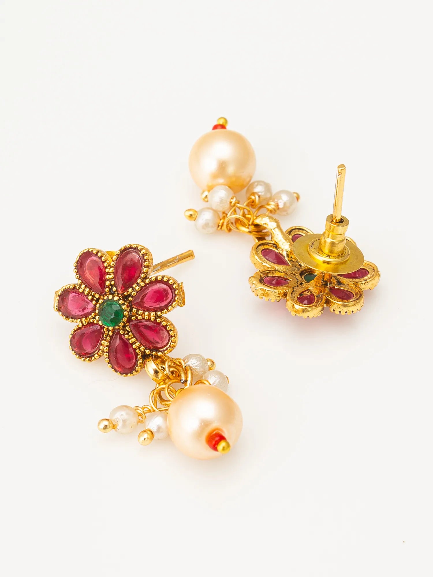 A pair of gold-plated floral drop earrings featuring pinkish-red petal stones, a small green center stone, and dangling cream-colored pearls on a white background.