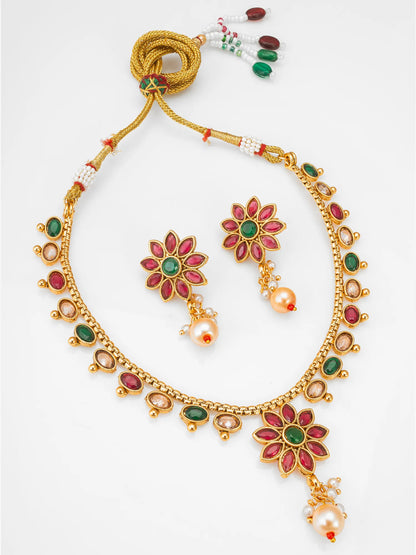 Gold-plated Indian jewelry set featuring a necklace, earrings, and a beaded cord accessory, decorated with red and green stones and white pearls on a white background.
