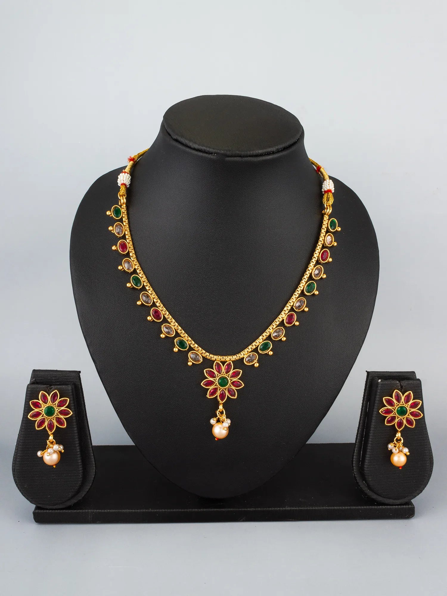Gold-plated floral jewelry set featuring a necklace and matching earrings displayed on a black mannequin bust and stand against a light gray background.