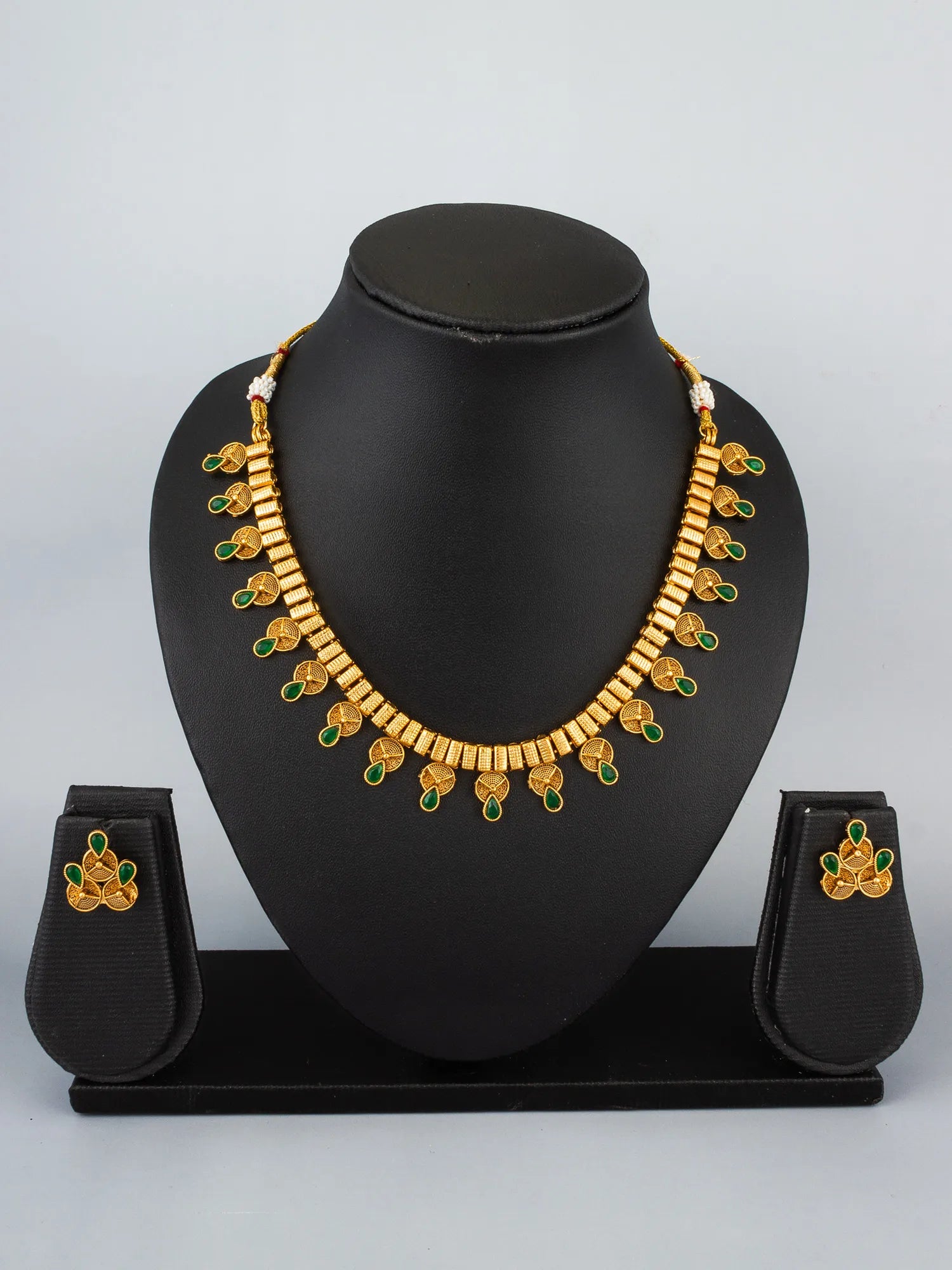 Gold necklace with green accents on a black mannequin bust against a gray background