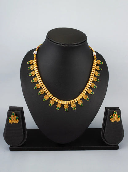 Gold necklace with green accents on a black mannequin bust against a gray background