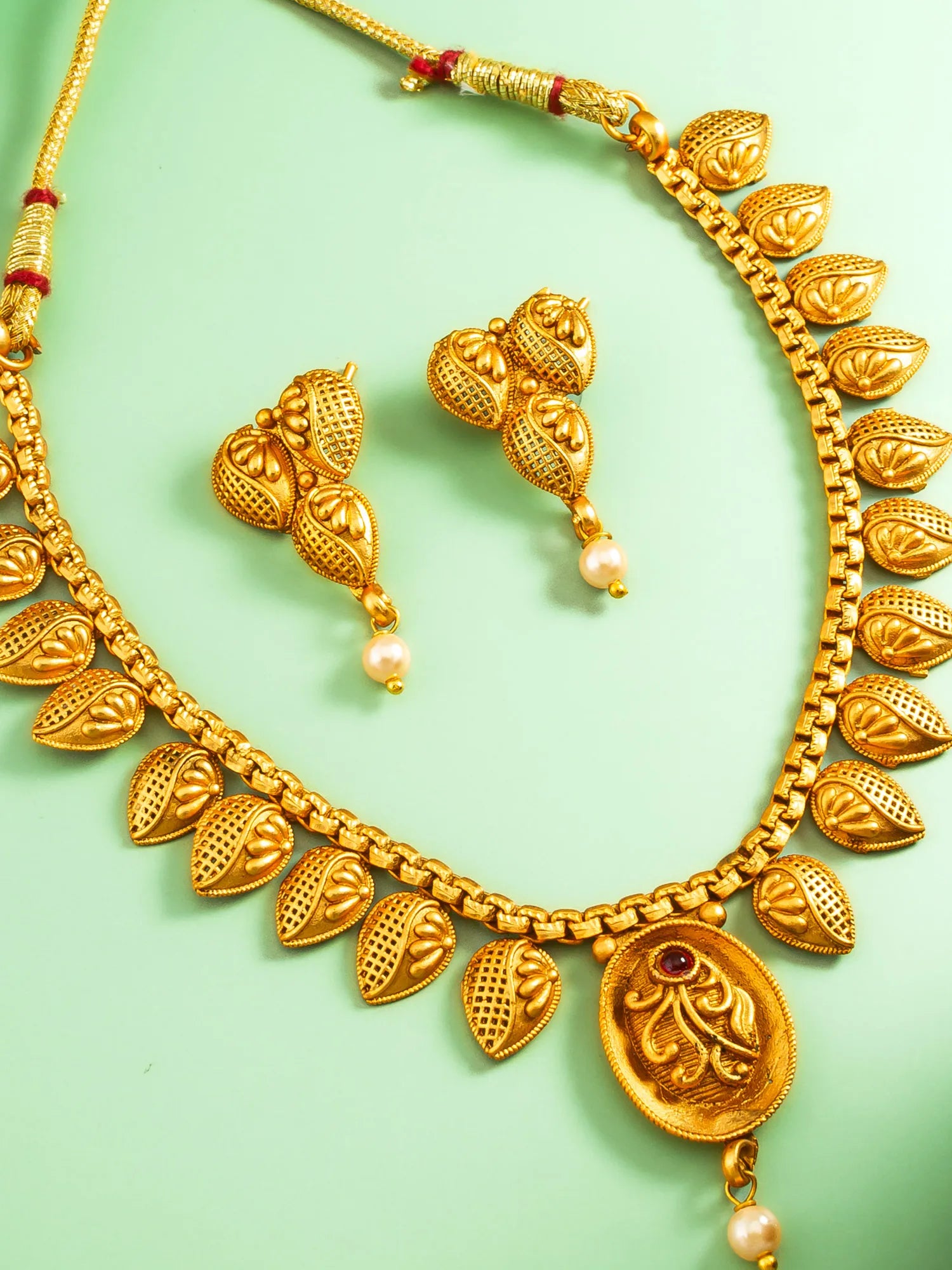 Gold necklace and earrings on a light green background