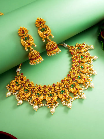 Gold necklace and earrings with gemstones on a green surface