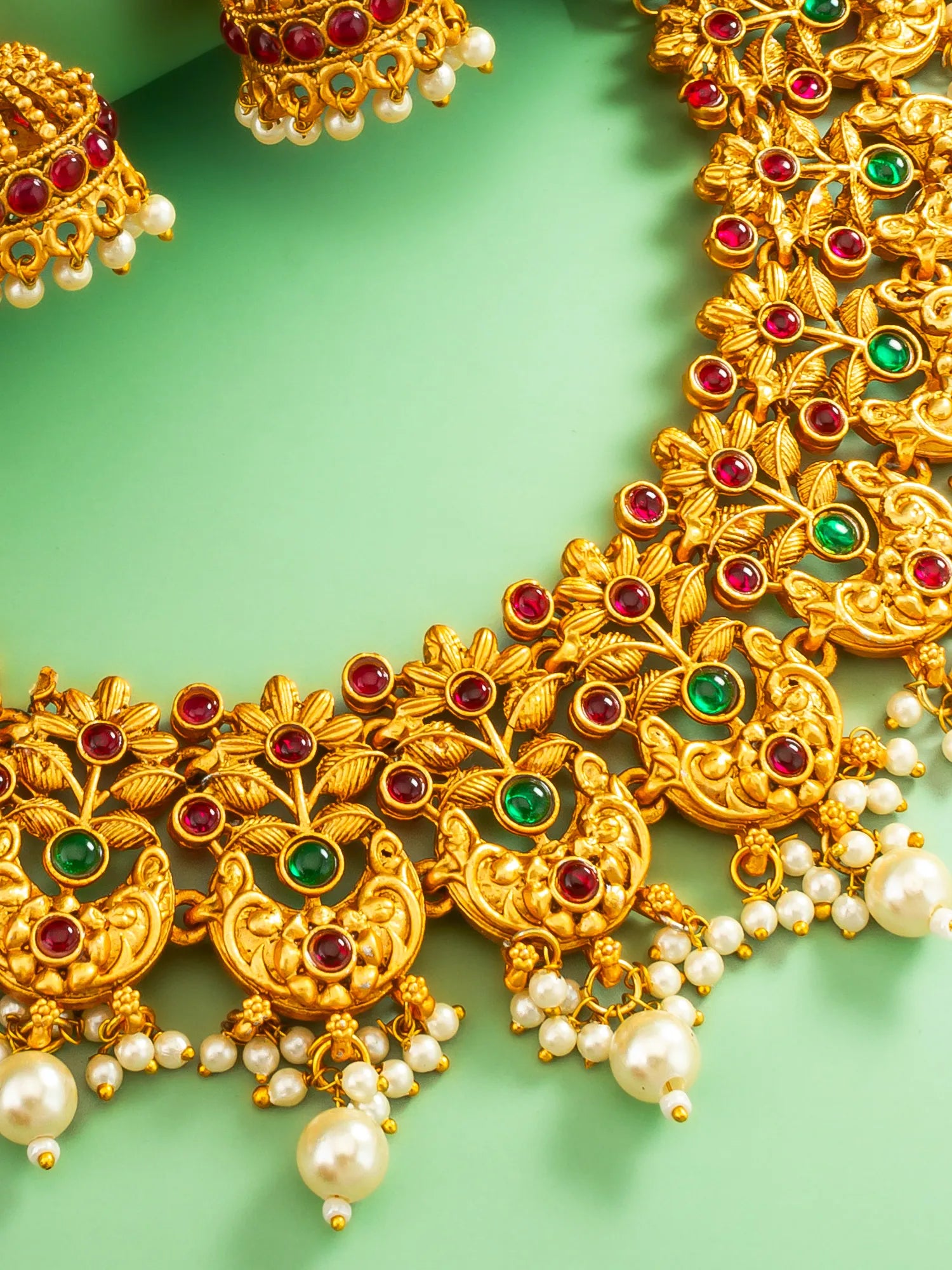 Gold necklace with red and green gemstones and pearls on a green background