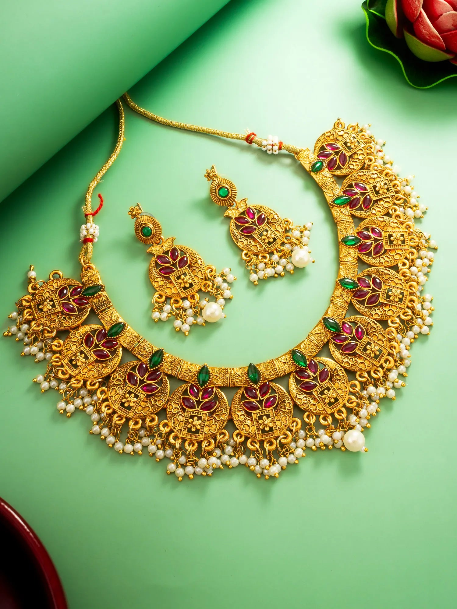 Gold necklace and earrings set on a green background