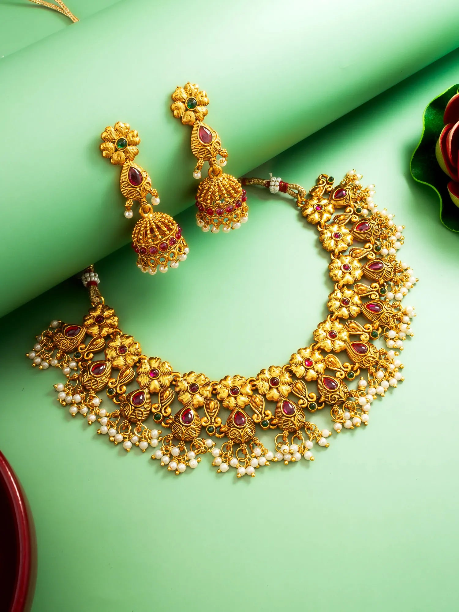 Gold necklace and earrings with red and green gemstones on a green background