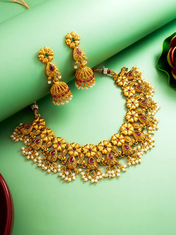 Gold necklace and earrings with red and green gemstones on a green background