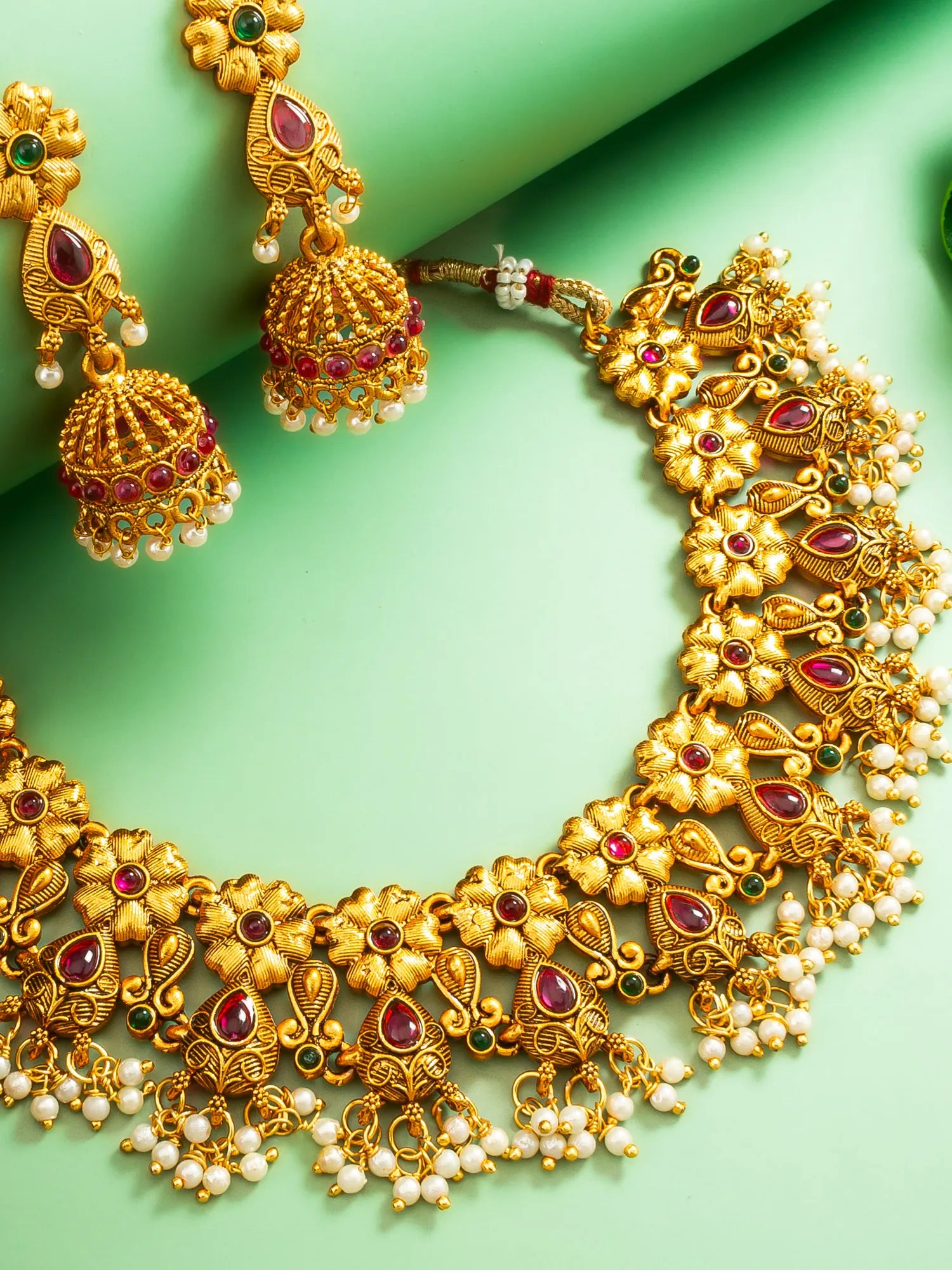 Gold necklace with red and green gemstones on a green background