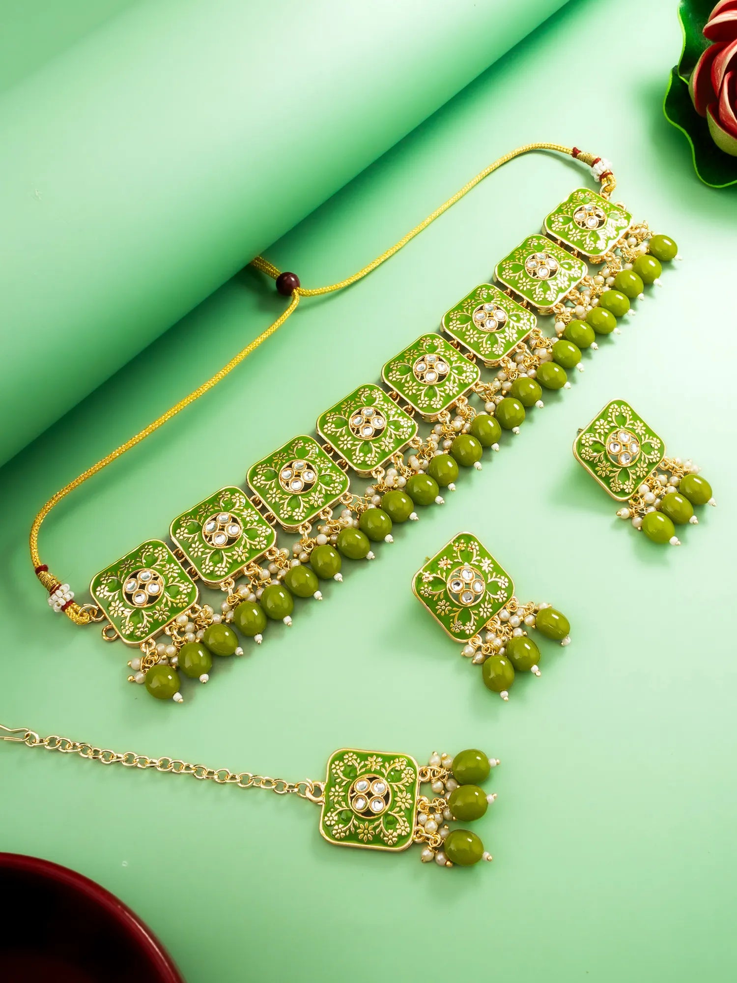 Green jewelry set with necklace, earrings, and bangles on a green background