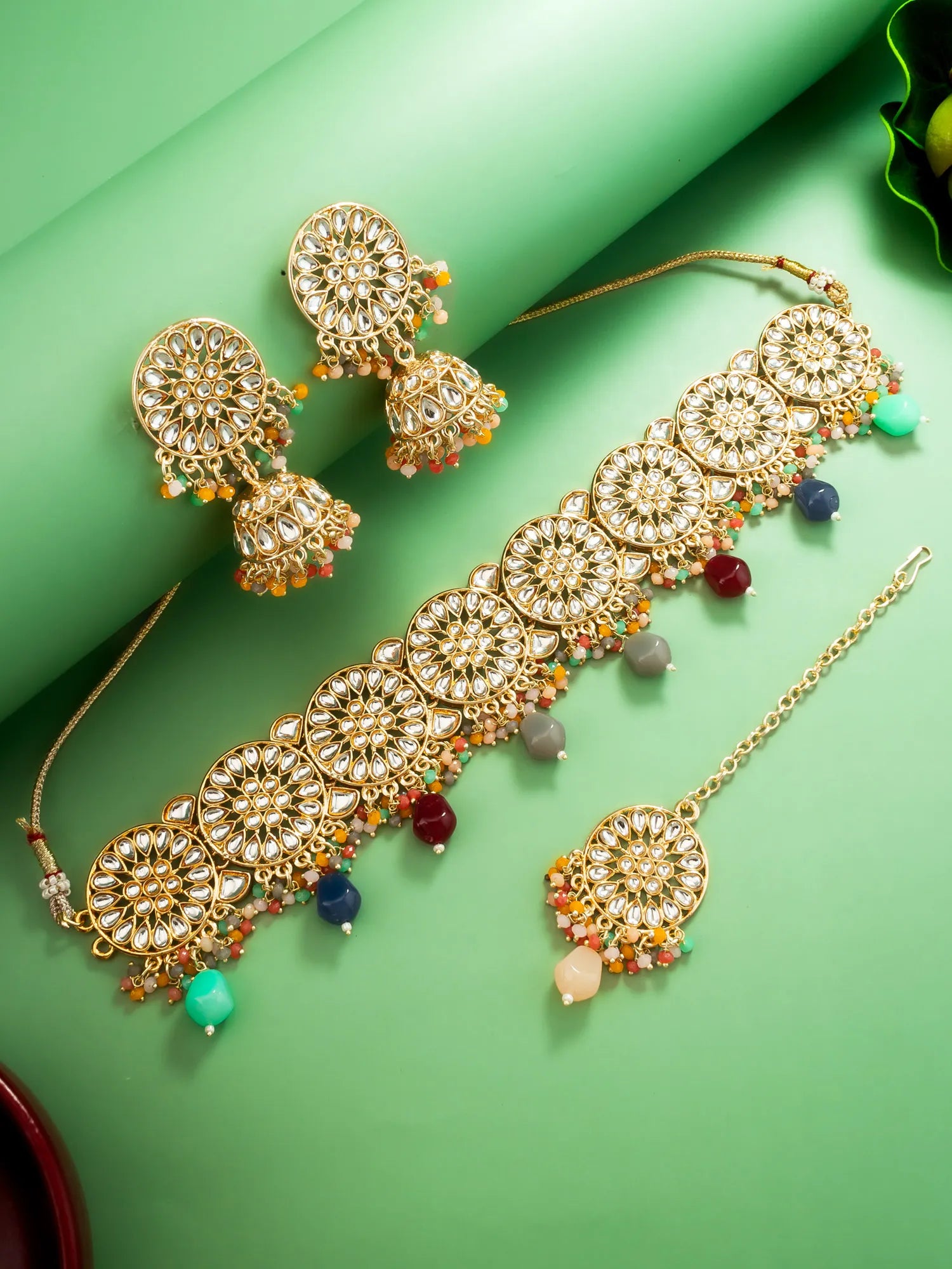 Ornate gold jewelry set with colorful beads on a green background