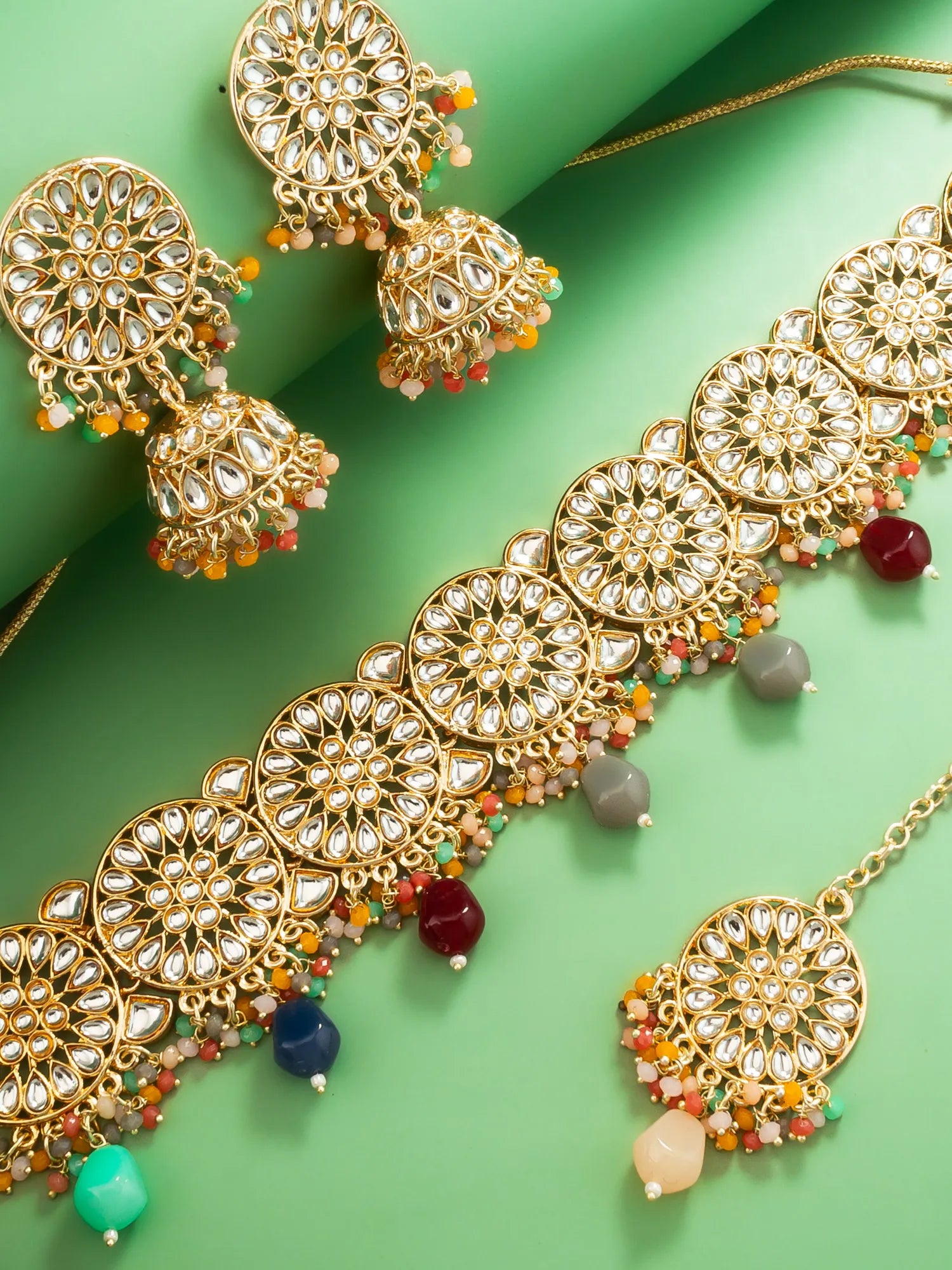 Gold jewelry set with colorful beads on a green background