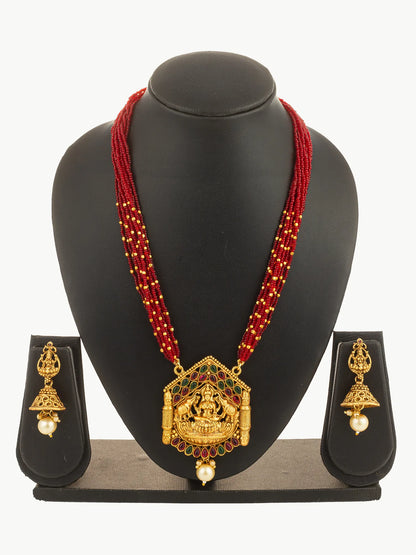 Gold necklace with red beads and matching earrings on a black stand