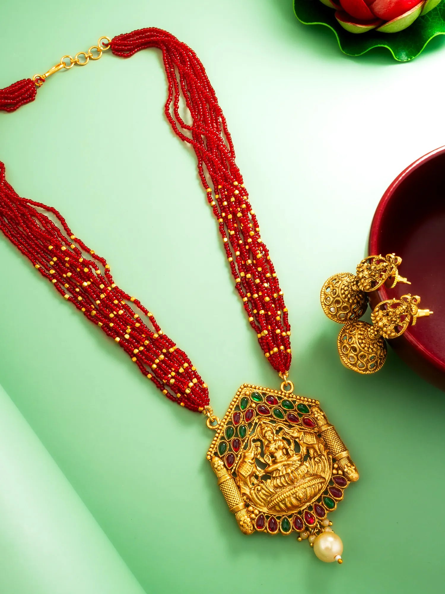 Gold necklace with red beads and green gemstones on a light green background