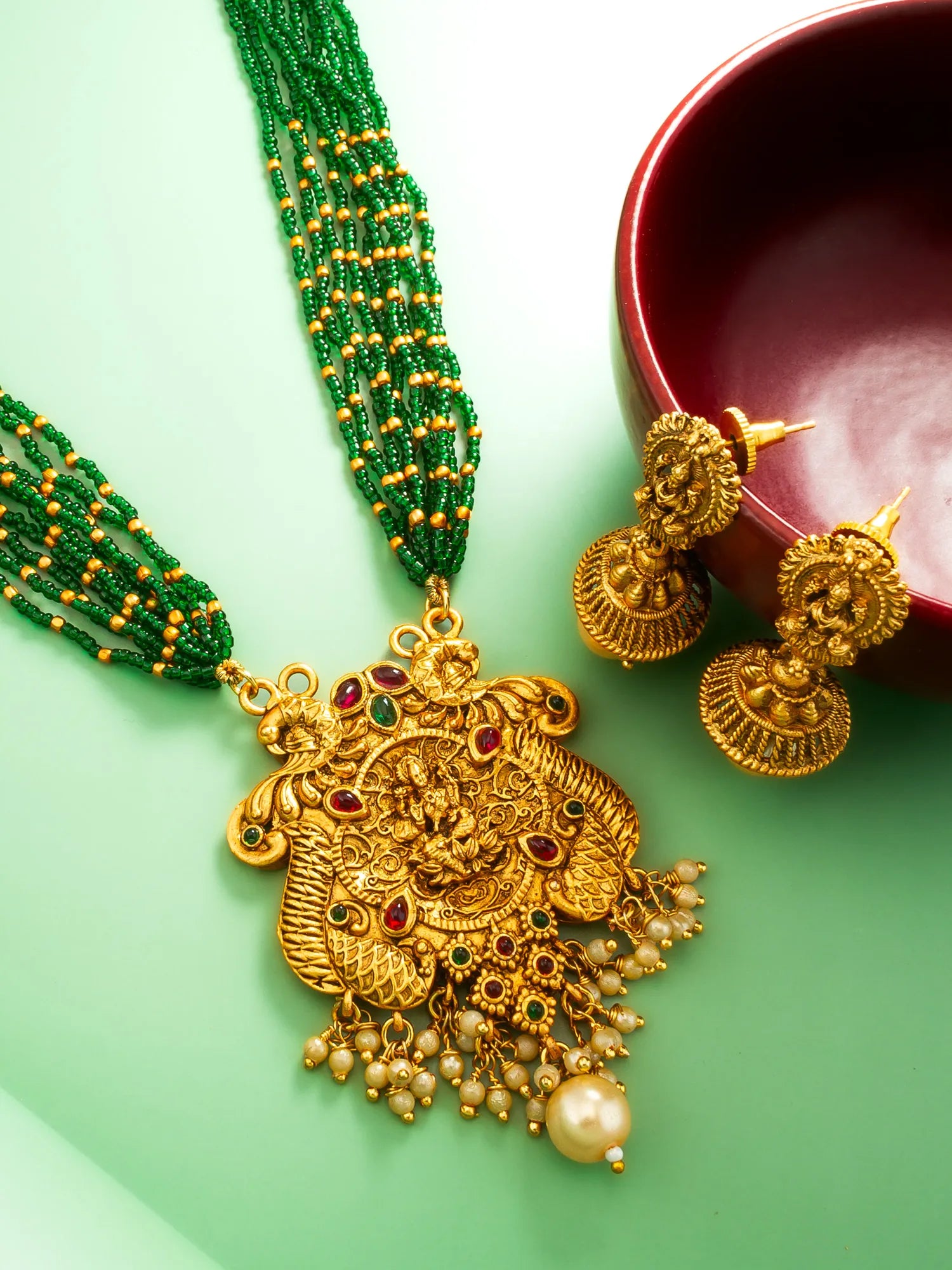 Gold necklace with green beaded chain and gold earrings on a light green background