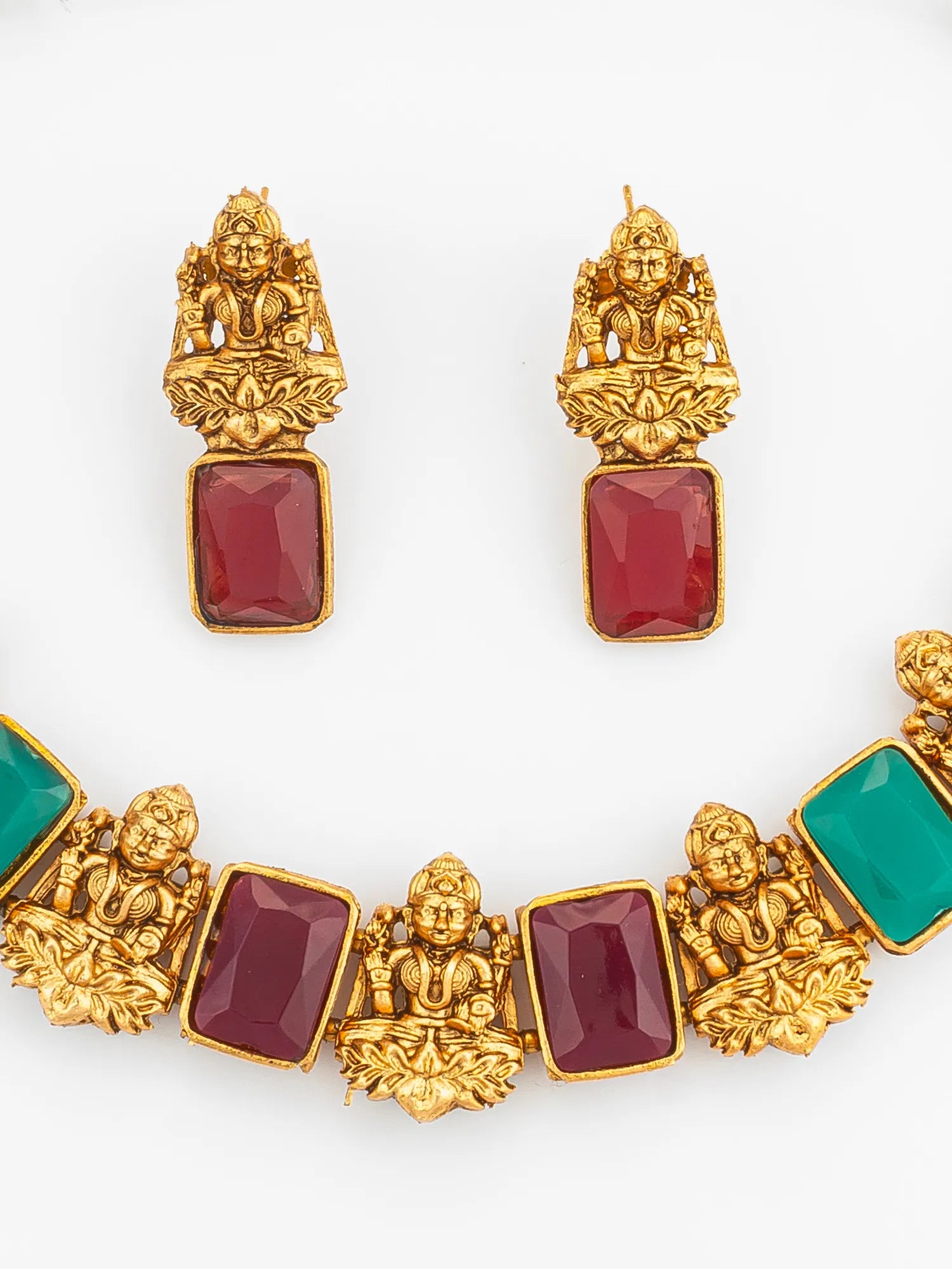 Ornate gold jewelry set with red and green stones on a white background