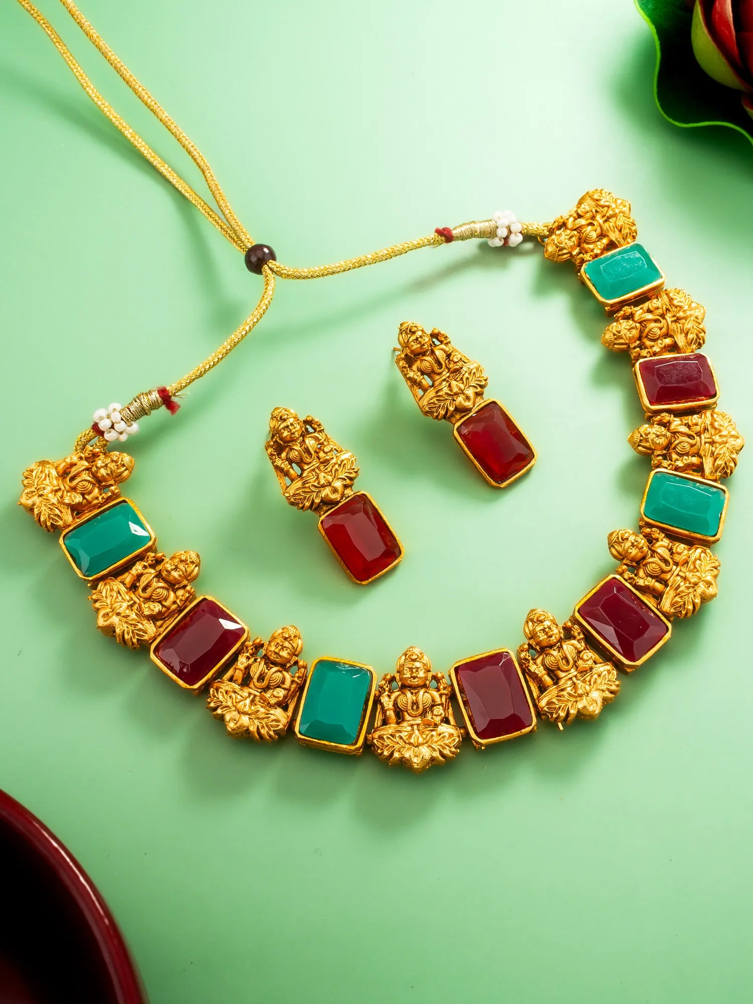 Gold necklace with red and green gemstones on a green background