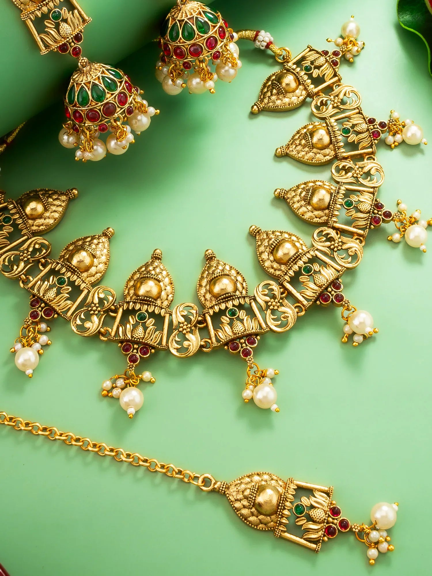 Gold necklace with pearls and gemstones on a green background