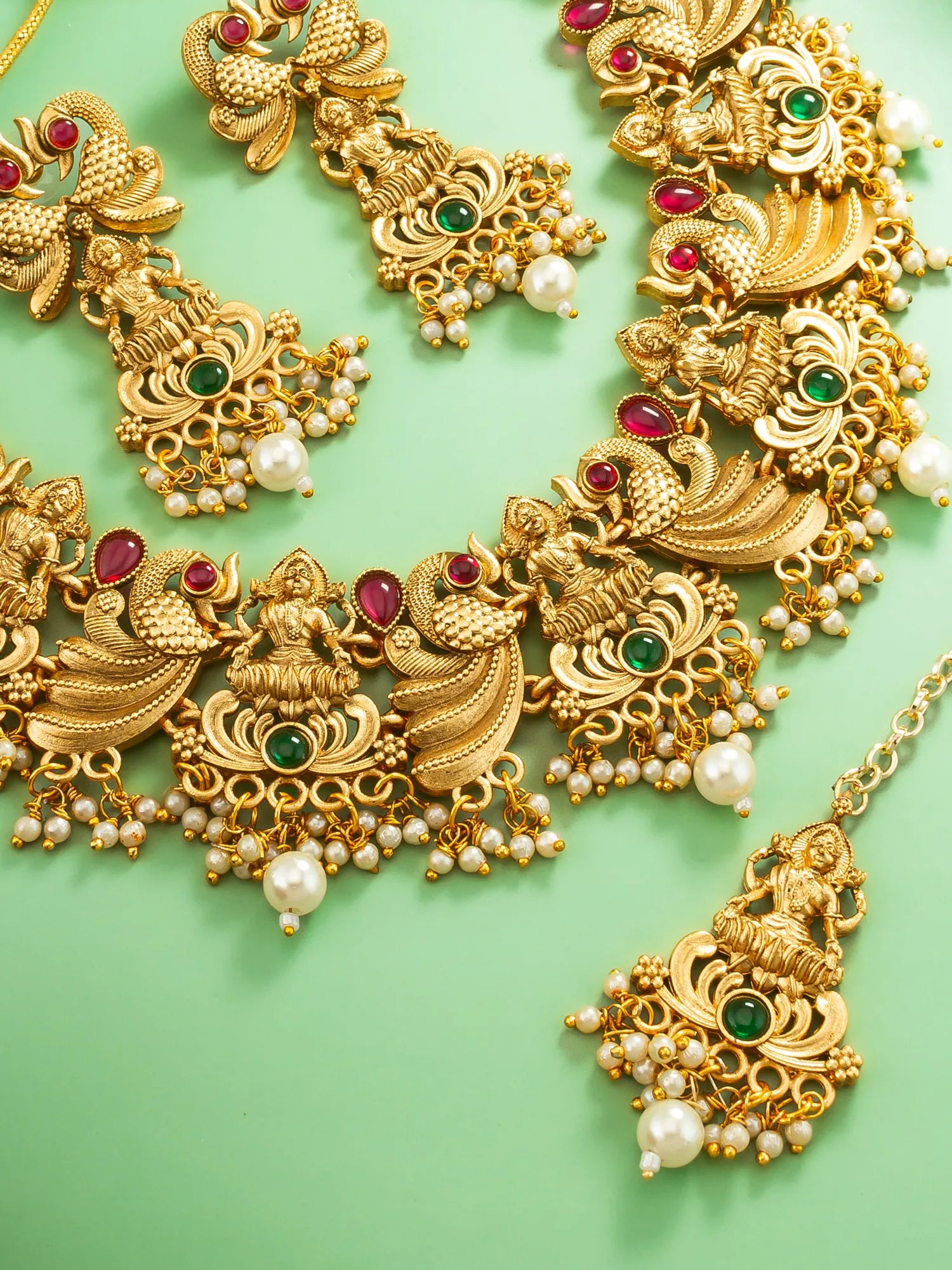 Ornate gold necklace with gemstones and pearls on a green background