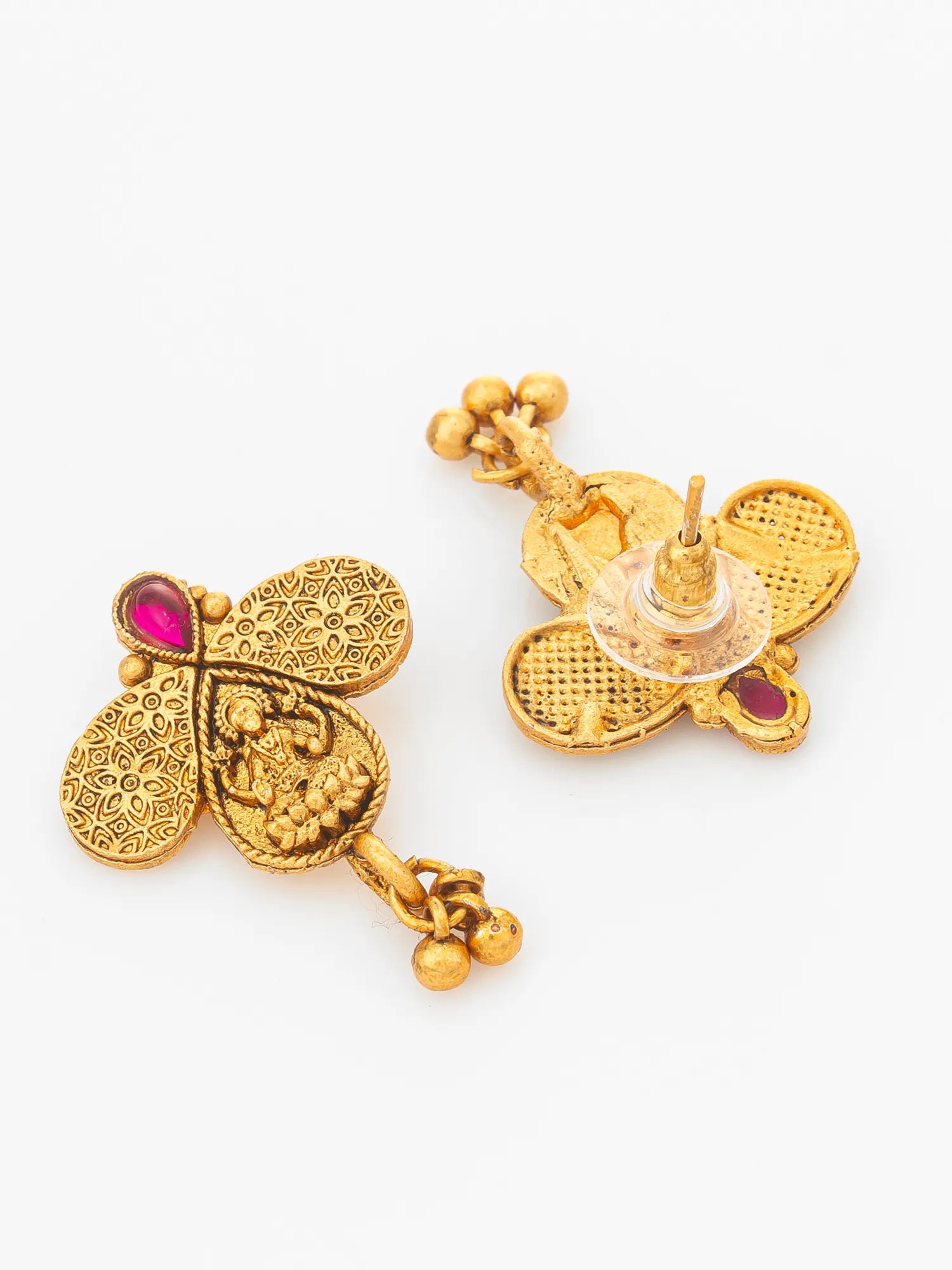 A pair of gold-toned traditional Indian earrings with detailed filigree work, a small deity motif, and a pink gemstone accent, shown on a plain white background.