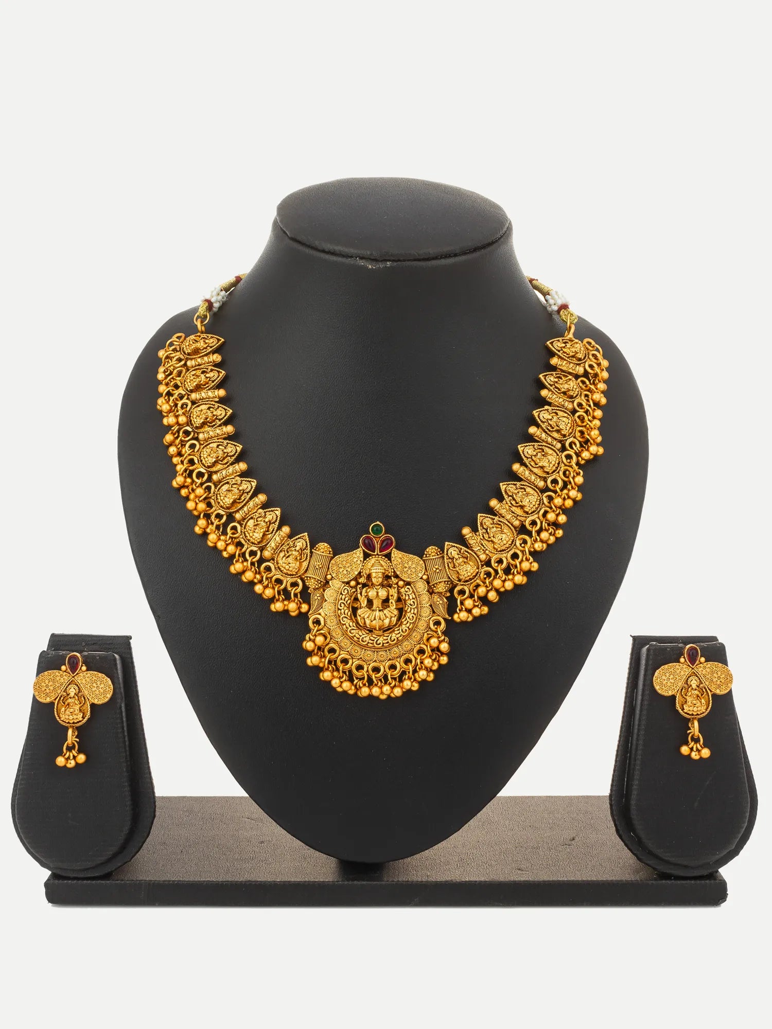 Gold-toned traditional Indian jewelry set featuring a statement necklace and matching earrings displayed on a black mannequin bust and stand against a light gray background.